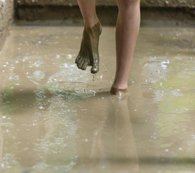 Ein Junge geht im Barfußpark durch ein Becken mit Matsch. (zu dpa «Barfußpark in der Heide startet in Saison») Foto: Philipp Schulze/dpa