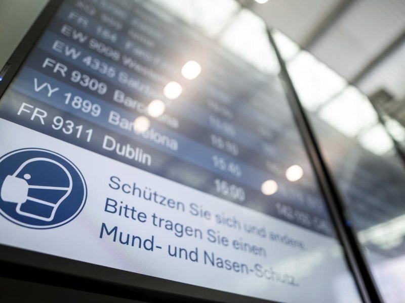 Auf einer Anzeigetafel im Flughafen steht der Hinweis «Schützen Sie sich und andere. Bitte tragen Sie einen Mund- und Nasen-Schutz». Die beiden großen Flughäfen in Köln und Düsseldorf empfehlen Reisenden weiterhin das Tragen von Corona-Masken. Foto: Fabian Strauch/dpa