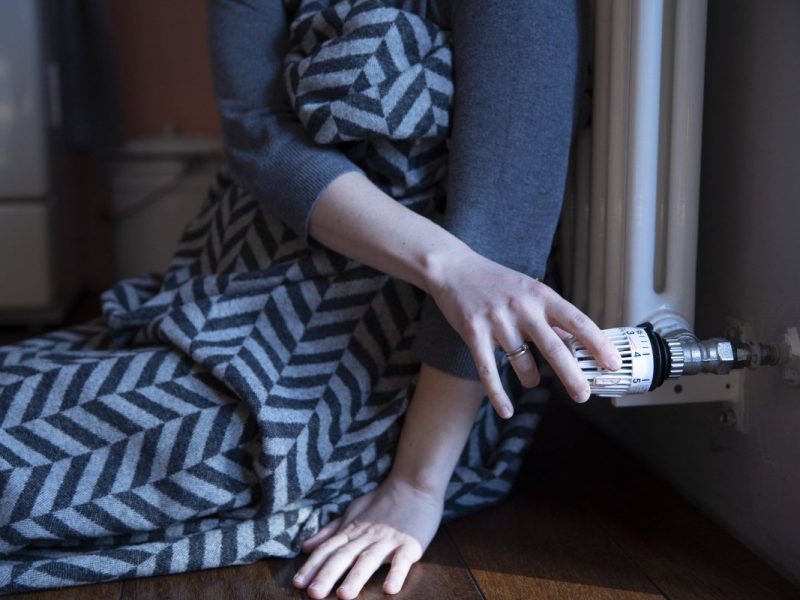 Frau sitzt vor Heizung in Decke eingewickelt