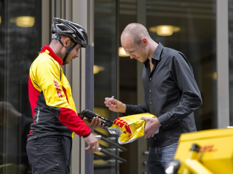 DHL-Fahrradkurier übergibt Kunden ein Paket, der unterschreibt