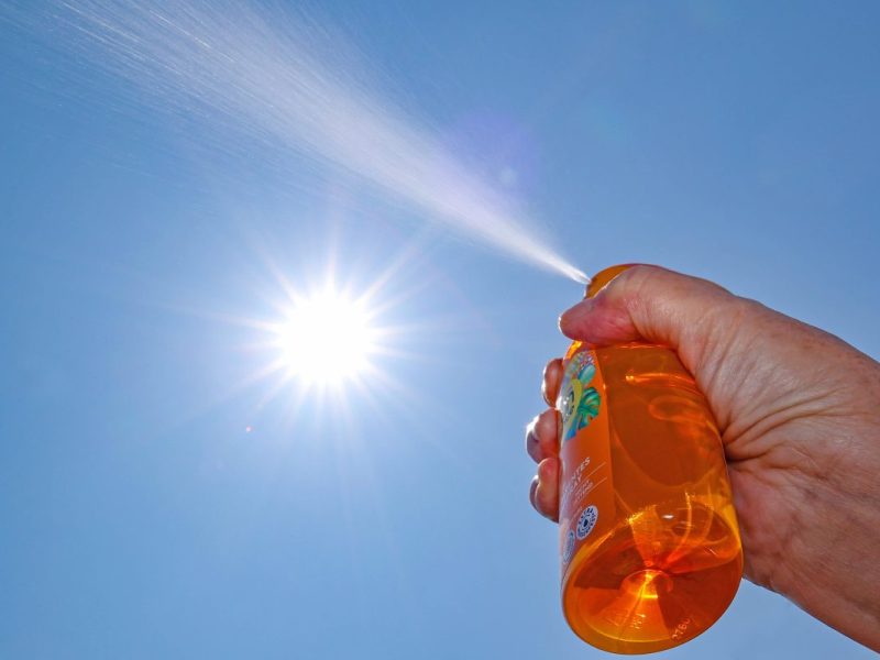Sonnenschein, klarer Himmel, Hand sprüht Sonnenspray aus Dose