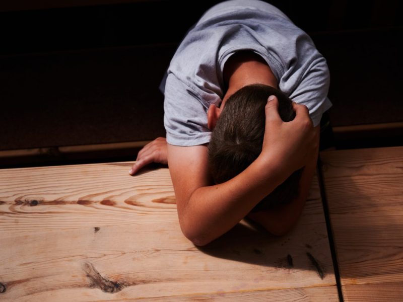 Kind stützt sich auf Arm auf Tischplatte ab