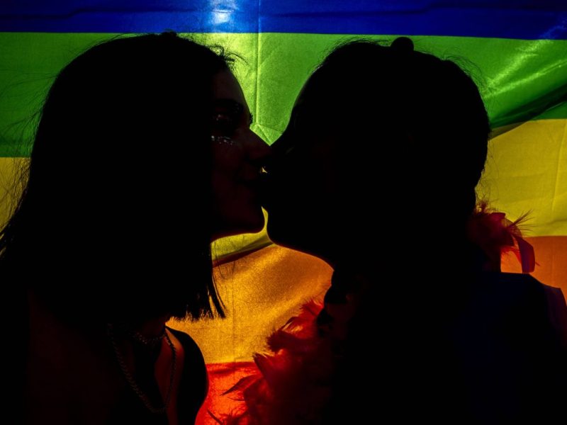 Zwei Frauen küssen sich vor einer Pride-Flagge