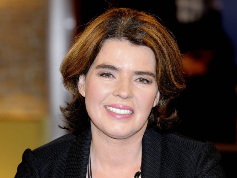 Auf dem Bild ist Fernsehmoderatorin Susanne Daubner zu sehen. Sie hat braune schulterlange Haare. Sie trägt neben einem breiten Grinsen einen schwarzen Blazer.