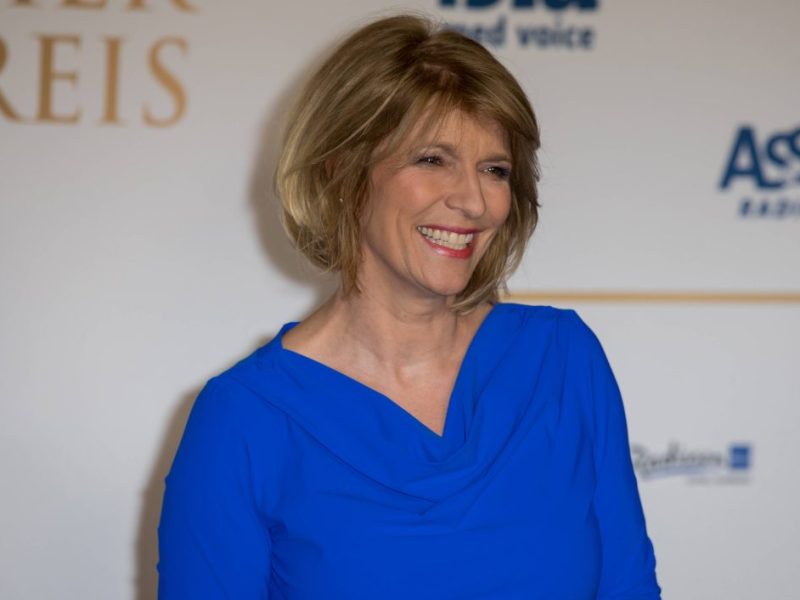 Auf dem Bild ist Tagesschau-Moderatorin Susanne Holst. Sie hat schulterlange blonde Haare. Zudem hat sie ein breites Grinsen im Gesicht und trägt ein königsblaues Kleid.